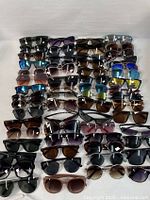 Top-down view showing 47 pairs of assorted sunglasses neatly arranged in rows, highlighting variety in frame styles and lens colors.