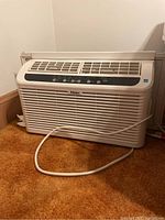Front view of Haier window air conditioner showing air vent grille, control panel, and power cord on carpet floor.