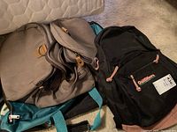Three bags: one black Outfitters backpack and two tan canvas overnight bags with turquoise accents