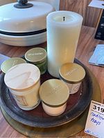 Photo of 6 candles, including one large white pillar candle and 5 Opalhouse branded candles in glass jars with gold lids, arranged on a round metal tray.