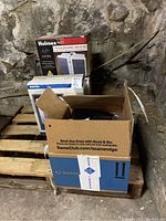 Photo of all items boxed and arranged on a wooden pallet against stone wall, showing the Homes ceramic heater box, Boston fan box, and the black box with the coffee pot inside a Sam's Club shipping box.