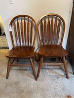 Front view of two wooden dining chairs with spindle backs and contoured seats on carpet.