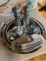 Top view of stainless steel salt and pepper grinders, sugar pot, creamer, butter dish, and portion of trays below.