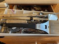 Drawer with barbecue utensils and flatware including wooden handle spatulas and spoons.