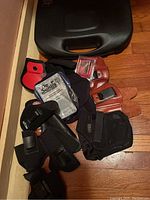 Lot displaying multiple holsters of leather, nylon, and molded plastic, with accessories including a black hard case and cleaning tools.