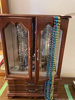 Front view of closed wooden jewelry box with colorful bead necklaces hanging on the right side