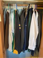 Closet view showing multiple men's clothing items on hangers including t-shirts and jackets in various colors and styles