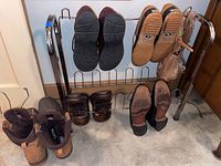 Multiple pairs of men's shoes on a metal shoe rack and a bag of shoelaces hung on the rack.