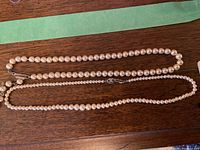 Two strands of pearl necklaces displayed on wood surface showing overall look and size difference.
