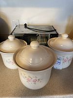 Three Pfaltzgraff canisters with floral design and three rounded lids. Oven Master toaster oven behind them.