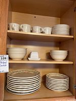 Wood cabinet shelf with multiple stacks of floral patterned plates, bowls, cups, and a butter dish.