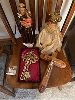 Photo showing two porcelain religious figurines and two religious crosses placed on wooden chairs. One gold-tone cross is boxed in red satin lining, the other is wooden with a gold crucifix attached.