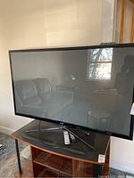 Front view of a 42 inch Samsung TV turned off, standing on a wooden table with a reflection of the room visible on the screen.