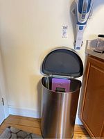 Tall stainless steel Simplehuman trash can with black sensor lid open, showing inside with a purple tag