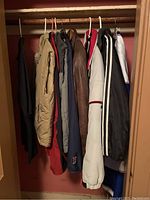 Full view of men's coats and jackets hanging in closet showing variety, colors, and materials including padded and leather styles.