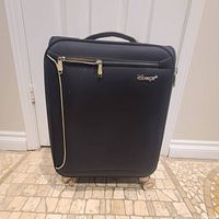 Closed black Verge carry-on suitcase with front zippered pocket and top handle.