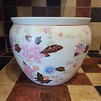 Front view of the white ceramic pot showing colorful floral and butterfly designs on the exterior surface.