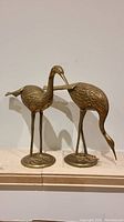 Pair of copper crane statues shown side by side, front view showing detailed feather texture and long legs.