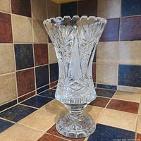 Photo showing the full vase on its pedestal base with the detailed cut glass patterns and scalloped rim visible.