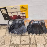 Two unopened sets of black Umbra Wisp drapery clip rings, each set contains 7 clips in original packaging.