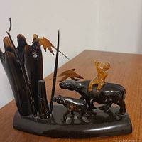 Photo of the decoration sculpture on wooden surface showing person riding buffalo, calf and reeds.