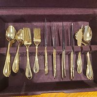 Close-up of all gold plated silverware pieces in velvet-lined box showing spoons, forks, knives and serving utensils