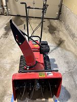 Front and top view of snowblower showing auger housing, track drive, chute and control handles inside garage