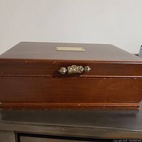 Closed view of the wooden jewelry box showing brass nameplate and carved knob