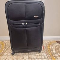 Front view of the black Samsonite expandable upright luggage showing two front zippered pockets and spinner wheels on the floor.
