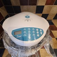 Top overview photo showing white lid control unit with blue digital keypad and display screen, sitting on the glass bowl wrapped in plastic.