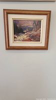Photo of the unsigned oil painting hanging on a white wall, showing landscape art and wooden frame.