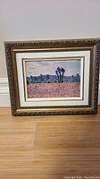 Frontal photo of the framed unsigned oil painting showing details of the floral field, trees, sky, and frame design.