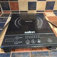 Black Salton induction cooker placed on a tiled surface showing top and control panel with power and temperature controls, digital display, and power cord on the right side.