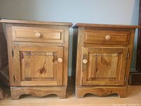 Frontal view of two solid oak night tables side by side, showing drawer and cabinet doors with wooden knobs.