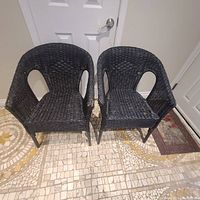 Two black wicker chairs side by side showing overall condition. One chair on the right has evident damage on seating area.