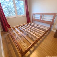 Front angle view of wooden queen bed frame, showing slatted wooden base and wooden frame with metal bars in the headboard.