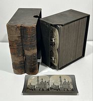Two leather-bound volumes with embossed spine titles alongside black storage box and single stereoview card laid flat