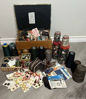 Wide view of entire collection including storage stool, jars of buttons, thread spools, and sewing notions packed in wooden box and scattered on floor