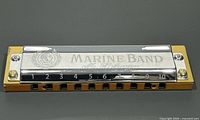 Close-up front view of the oversized Hohner Marine Band harmonica display, showing engraved metal top and yellow wooden base with black numbering and holes.
