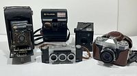 Front view of six vintage cameras including Polaroid Sun 660, Ansco Cadet Film Box No3, Kodak Model H, Zeiss Ikon Contaflex, Stereo Realist with David White lenses, and another box camera.