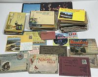 Image showing multiple stacks of assorted vintage souvenir postcards and postcard sets, with visible titles including Niagara Falls, Prince Edward Island, and Muskoka. The postcards are mostly landscape format with some in small folders or albums.
