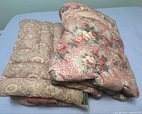 Two folded vintage bedspreads stacked, showing floral and paisley pattern visible edges.