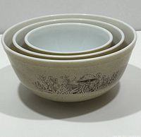 Stacked nested view of the full set of three vintage Pyrex Forest Fancies mushroom pattern mixing bowls, showing the patterned exterior and white interiors.