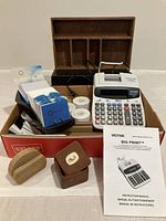 Full view of lot showing Victor Big Print adding machine, instruction manual, Rolodex, stone business card holder, small box with scrimshaw decoration, wooden organizer, and thermal paper rolls arranged on a white surface.