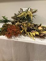 Collection of artificial flowers including autumn swags with various colors and textures laid out on a table.