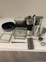 Image showing all items on a table with two Bundt pans, glass dishes, aluminum pots, tea strainers, and fish spatula visible.