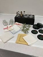 Table setting with salt and pepper shakers, linen napkins, napkin rings, butter dishes, and coasters arranged on white surface.