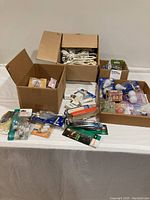 Photo showing three boxes containing mixed light bulbs, extension cords, and plugs on a white table.