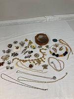 Full view of assortment of pins, necklaces, earrings, and brooches arranged around mid-century style shell-covered wooden box on white surface.