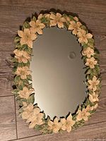 Front view of oval mirror with handmade decoupage floral frame showing paper flowers and leaves around the edge.